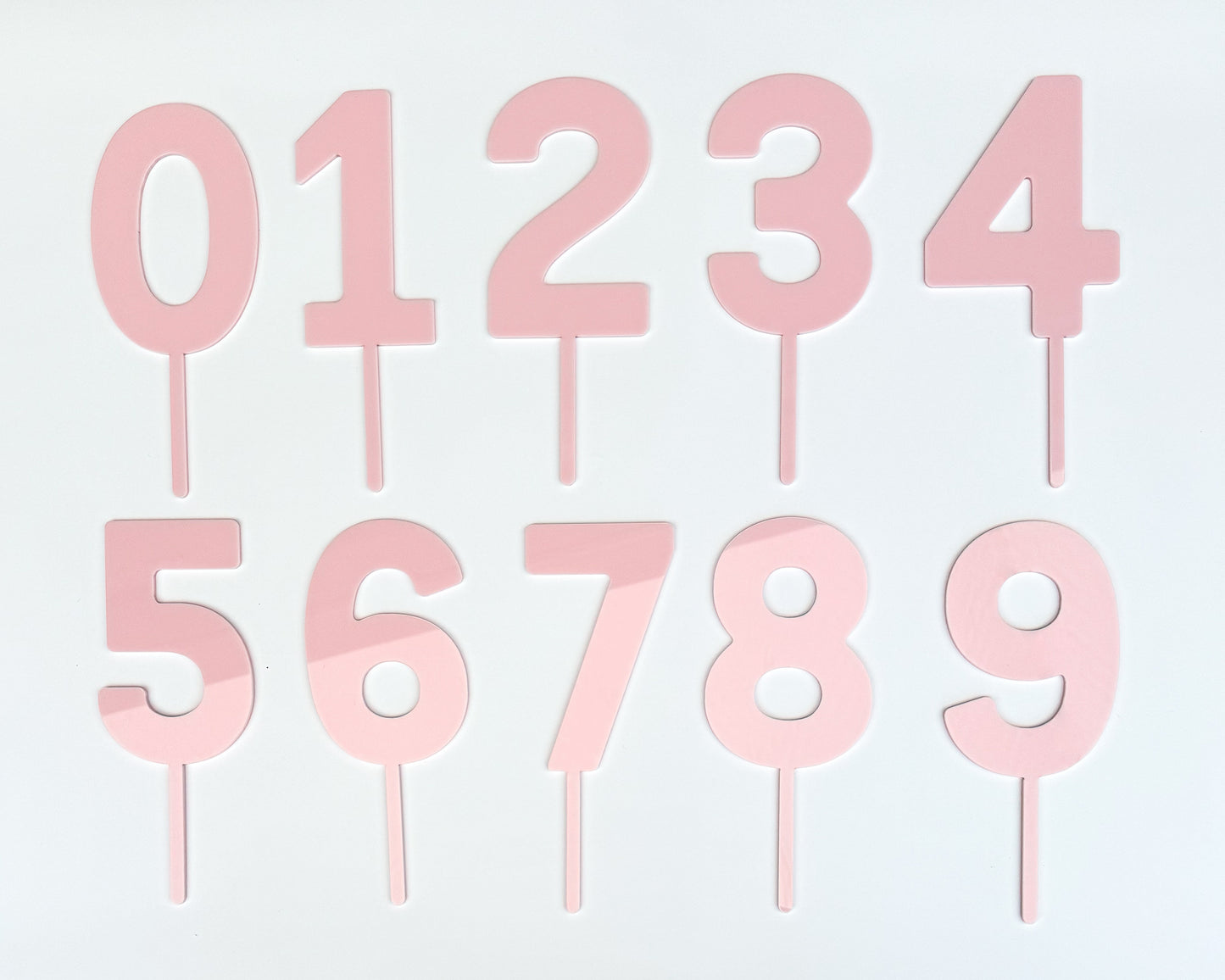 Set of blush pink number cake toppers on a light gray background
