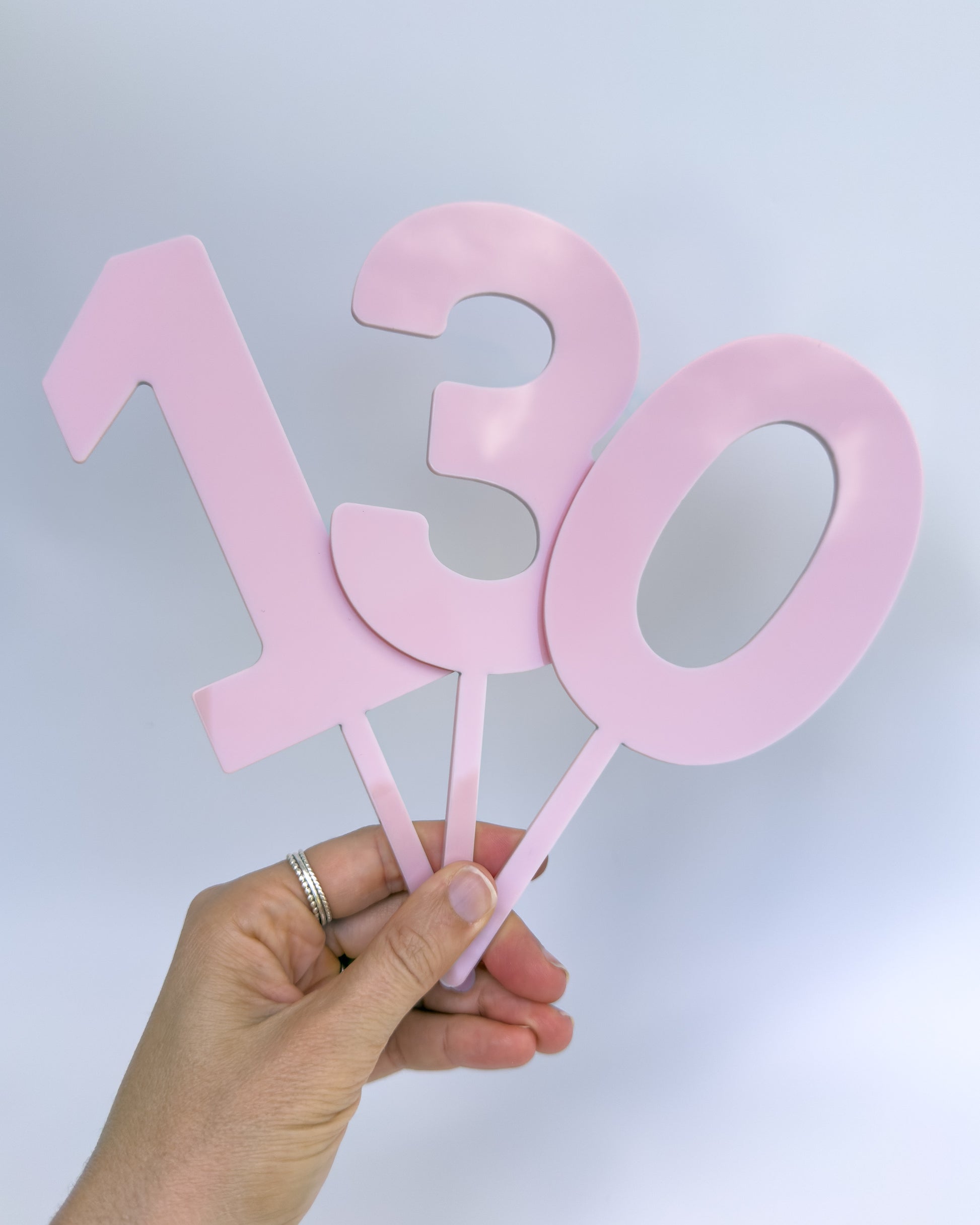 Hand holding blush pink number cake toppers