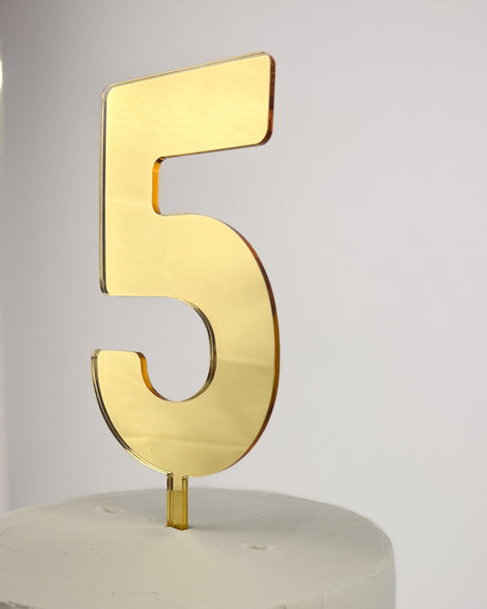 Gold number 5 cake topper on a white cake against a light gray background