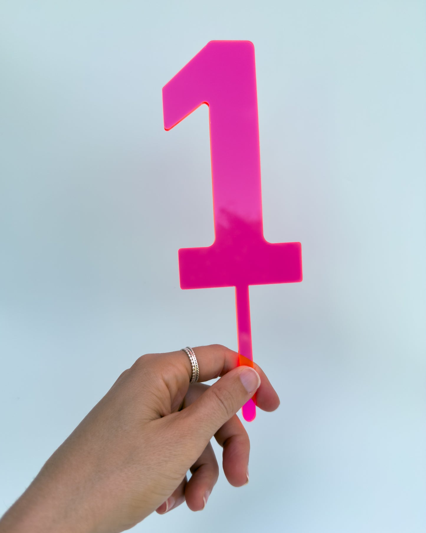 Hand holding a pink number '1' cake topper 